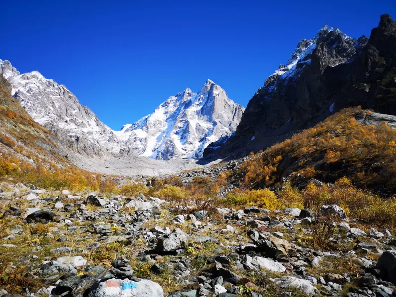 Rocky trail with a red-and-white waymark below granite peaks